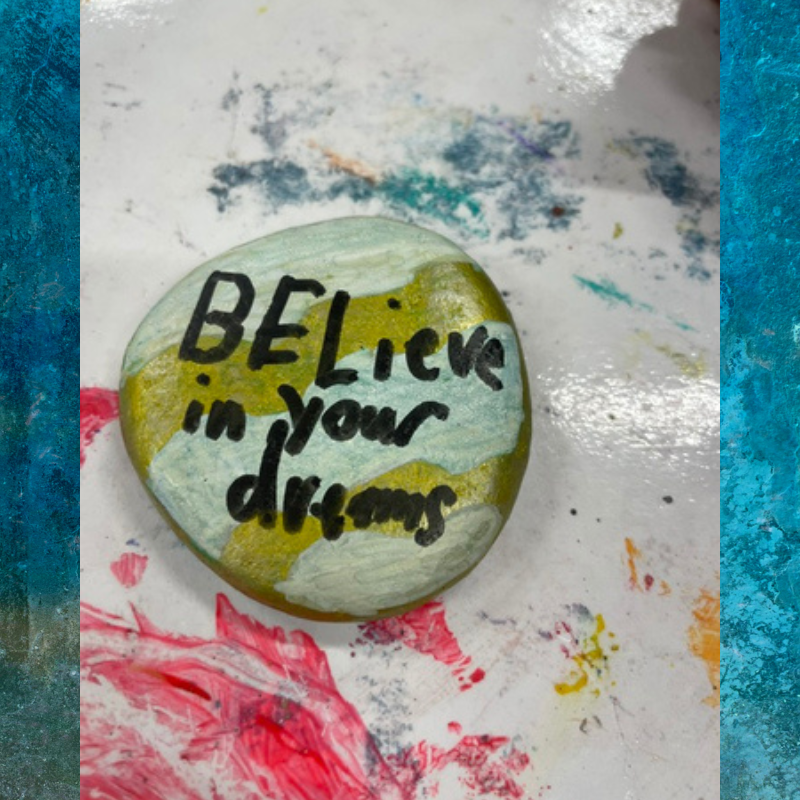 A painted rock with the words 'BELIEVE in your dreams' in black lettering.