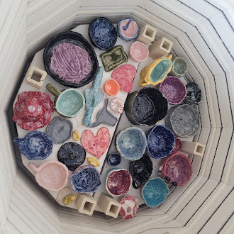 A kiln shelf is filled with an assortment of colorful, handmade ceramic pottery and bowls.