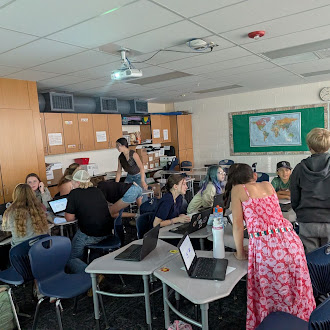 Students work at desks with laptops in a bright classroom with wooden cabinets.