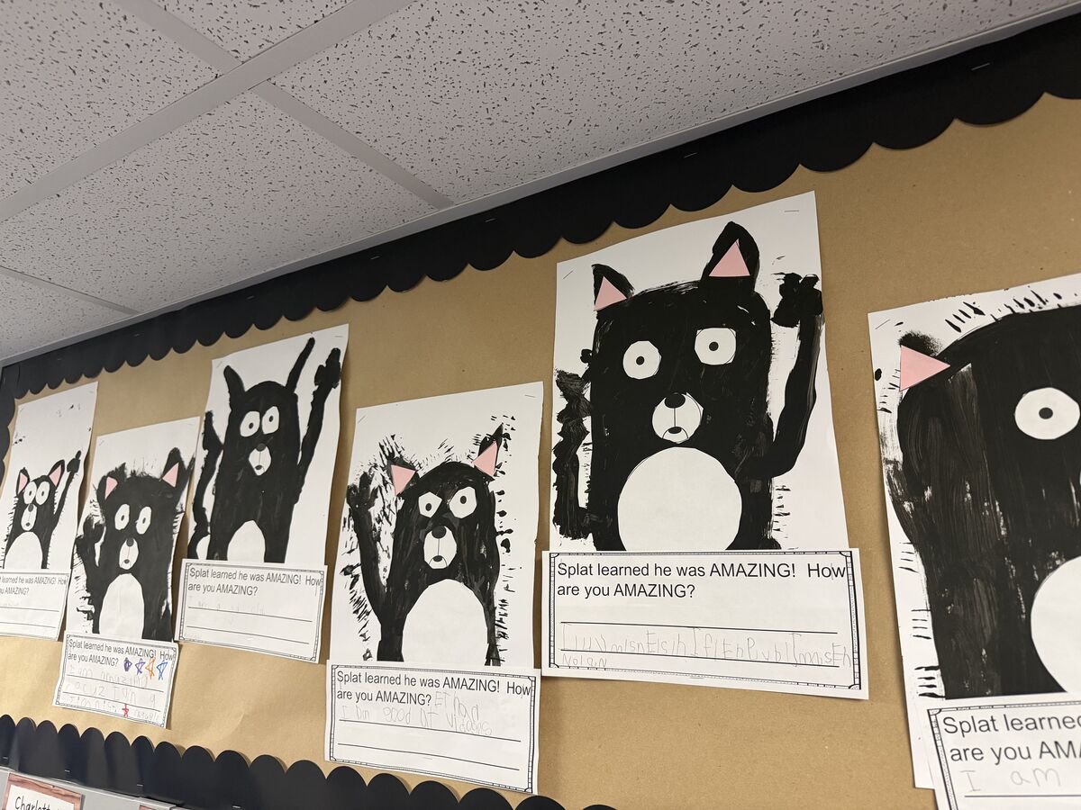 A classroom bulletin board displays children's artwork featuring painted black cats with pink ears.