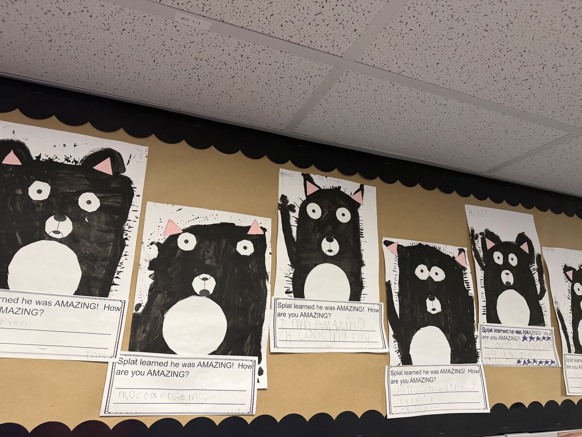 A classroom bulletin board displays students' black cat art projects with handwritten text reading 'Splat learned he was AMAZING!'.
