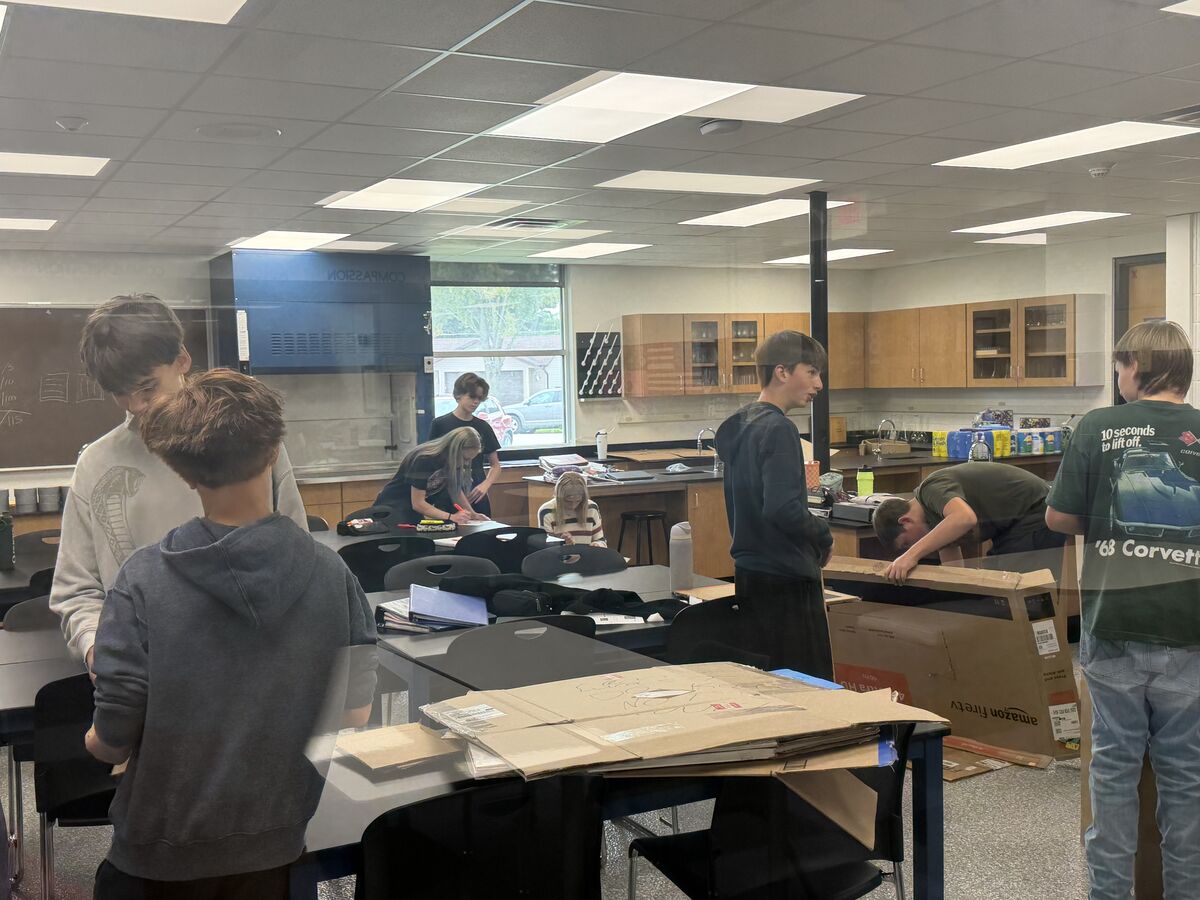 Students work on a project in a brightly lit classroom with tables and science lab equipment.