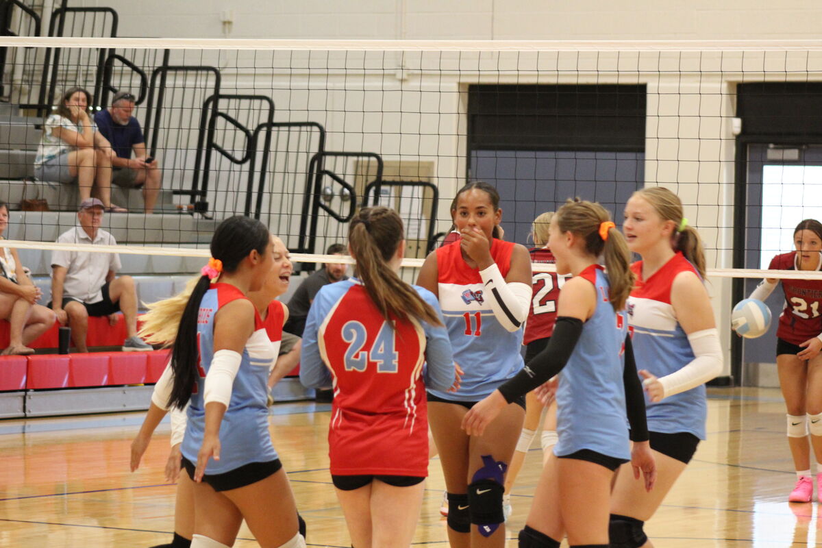 A high school volleyball team in blue and red uniforms celebrates on the court during a match.