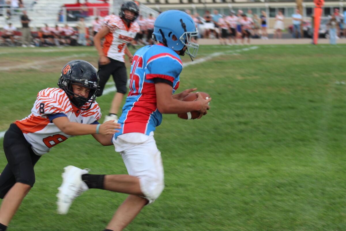 A youth football player in a blue and red uniform runs across the field with the football.