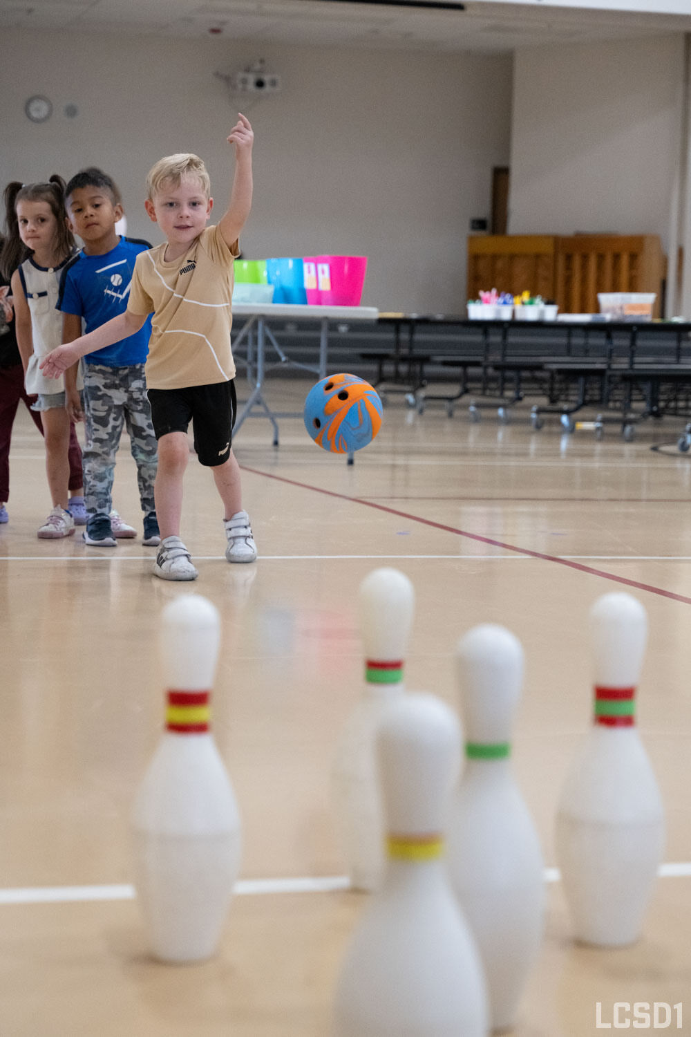 A young boy throws a bowling ball towards pins in a gymnasium.