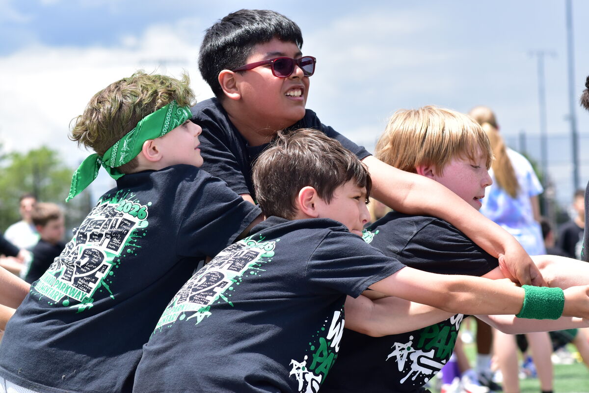 A group of children in black t-shirts with green designs are huddled together, appearing to be in a tug-of-war or team activity.