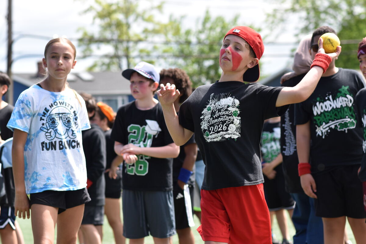 A boy with red face paint and a red cap throws a yellow ball during an outdoor event.