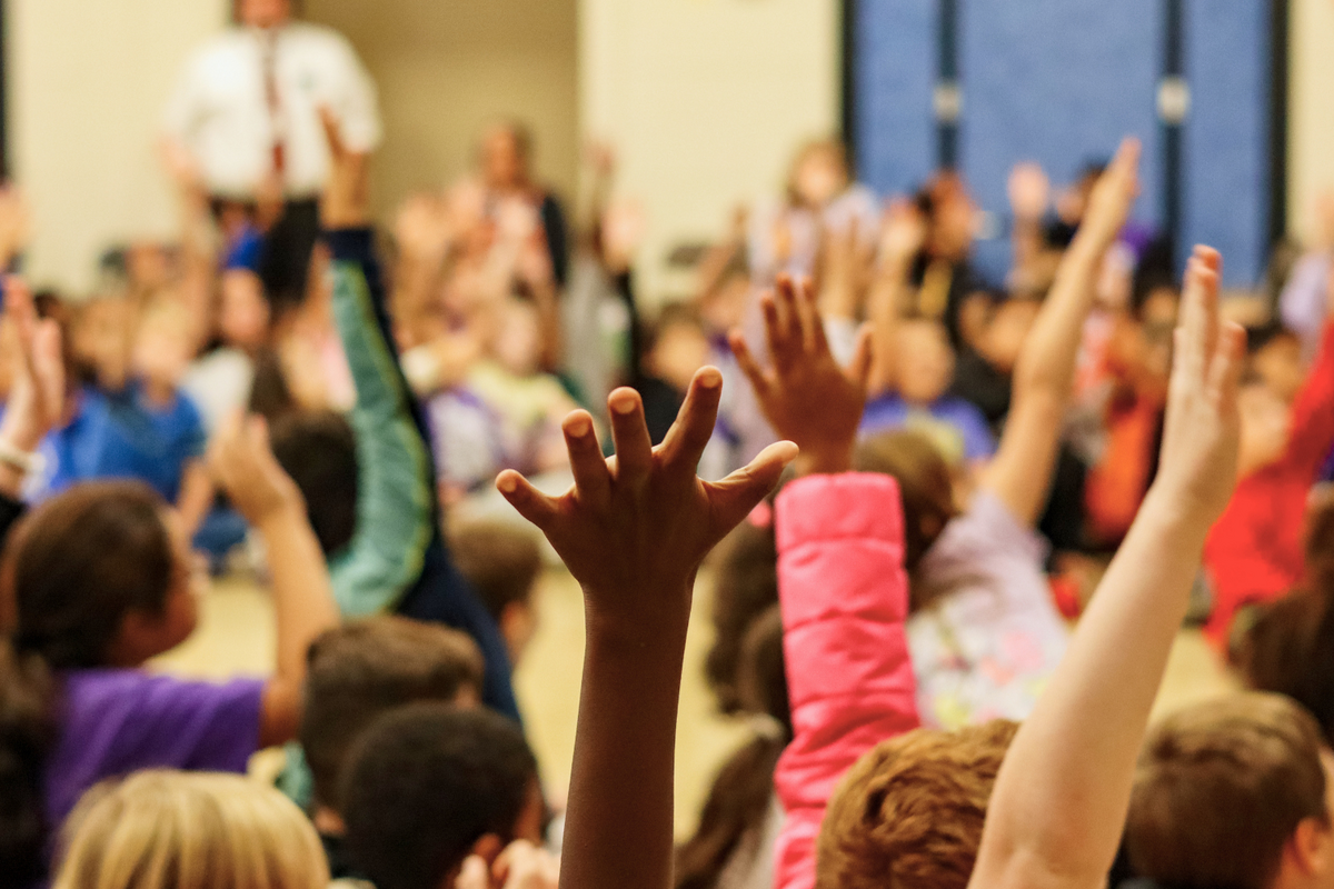 A group of students raise their hands high in a classroom setting.