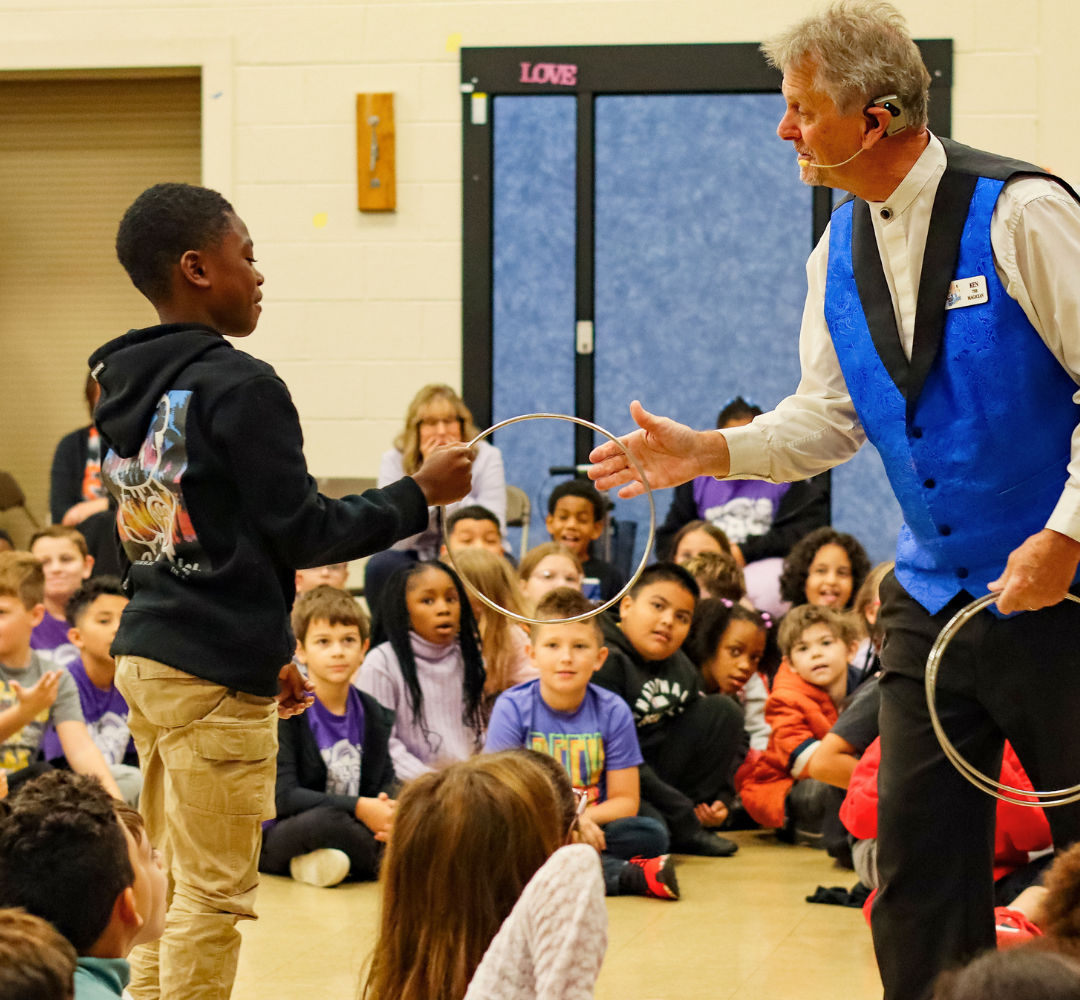 A magician in a blue vest performs a ring trick with a child volunteer.