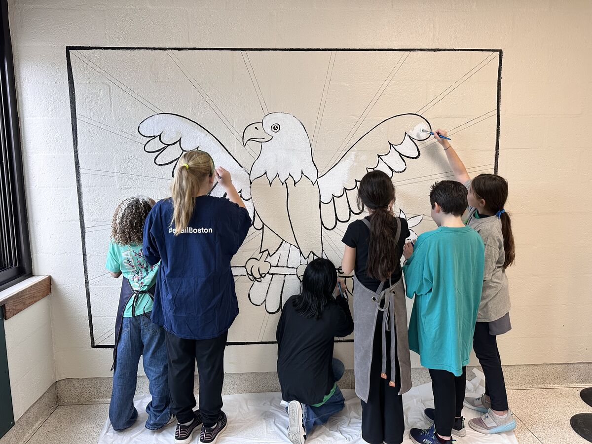 Children paint a large eagle mural on a white wall.