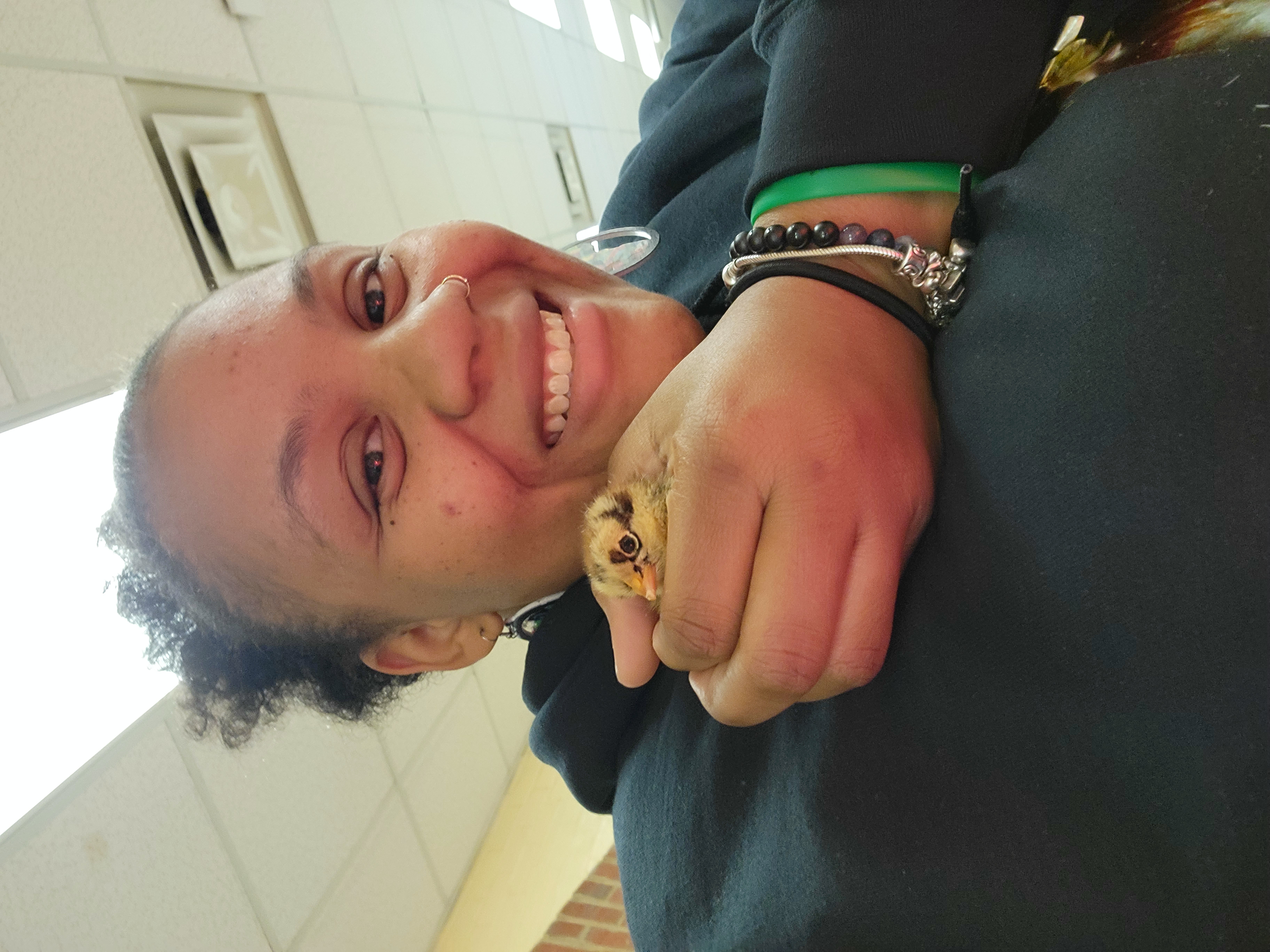 A smiling person gently holds a small, fluffy chick close to their face indoors.
