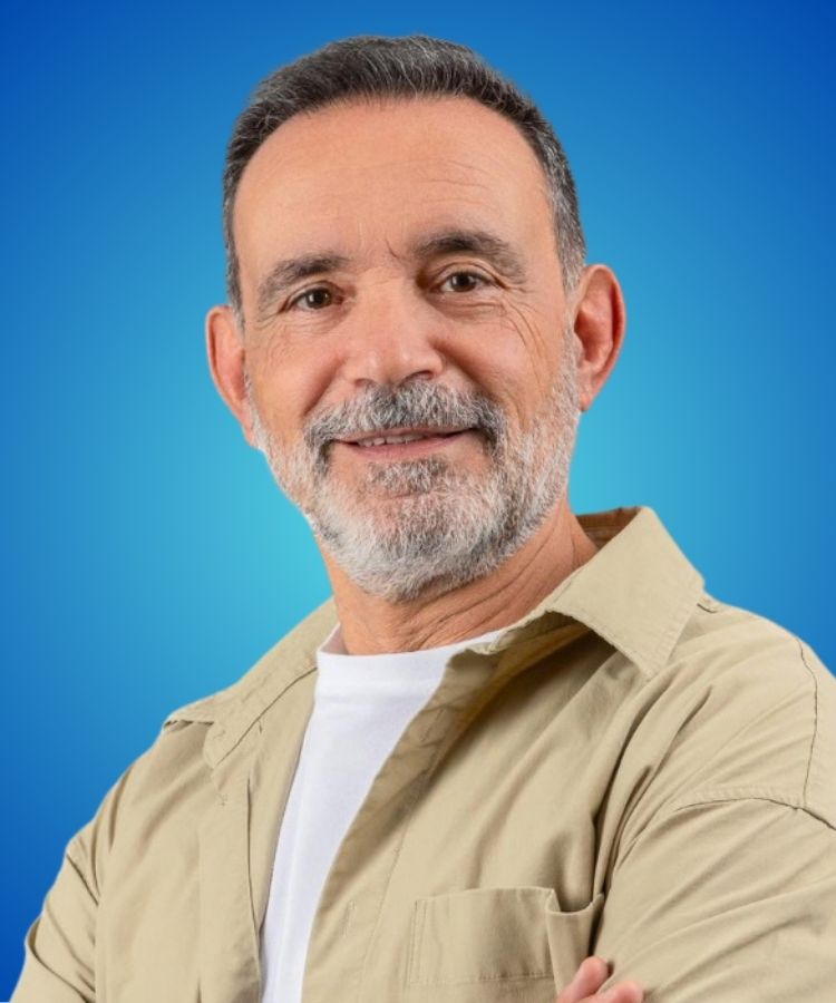 A smiling middle-aged man with short gray hair and a trimmed beard against a solid blue background.