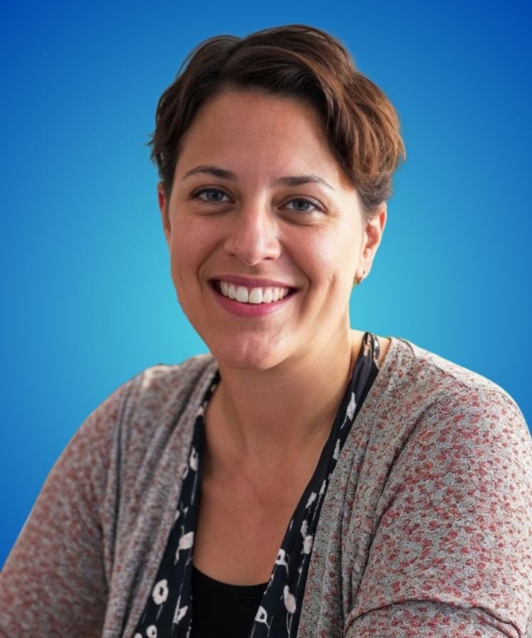 A smiling woman with short brown hair poses against a solid blue background.