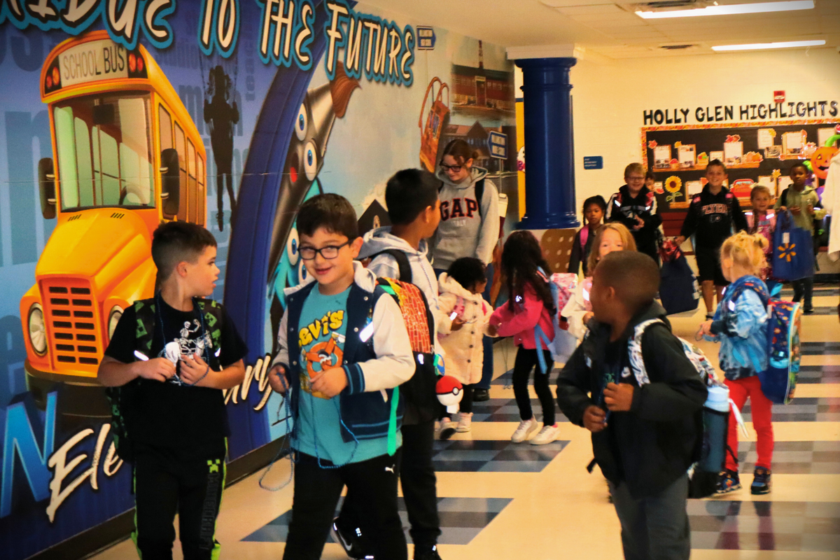 Students walk down a school hallway featuring a vibrant mural of a yellow school bus and the words 'To the Future'.