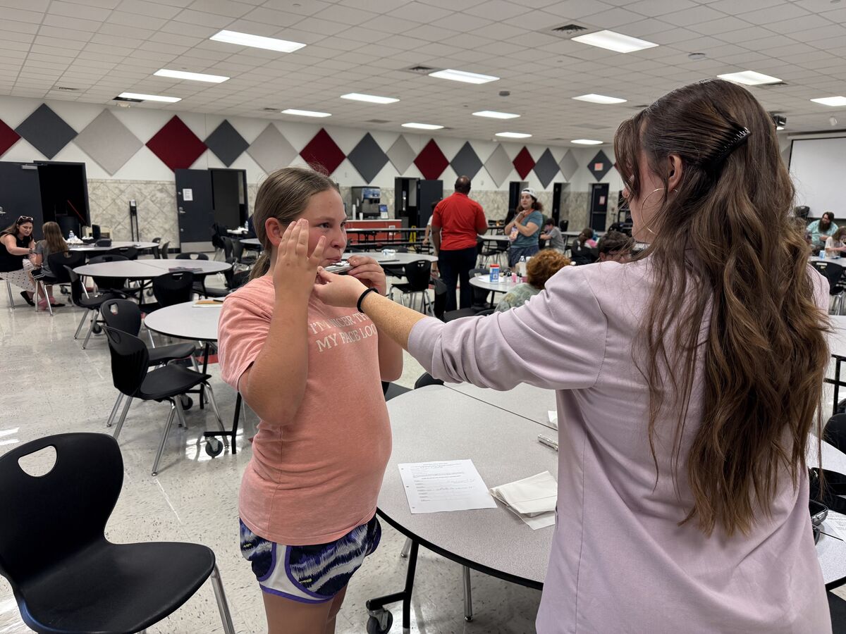 A teacher guides a student on how to hold a flute in a large cafeteria room.