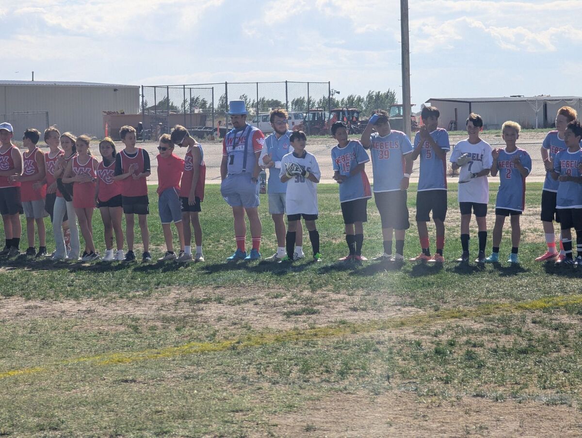A line of young athletes and coaches stands on a grassy field, wearing matching red and blue team jerseys.