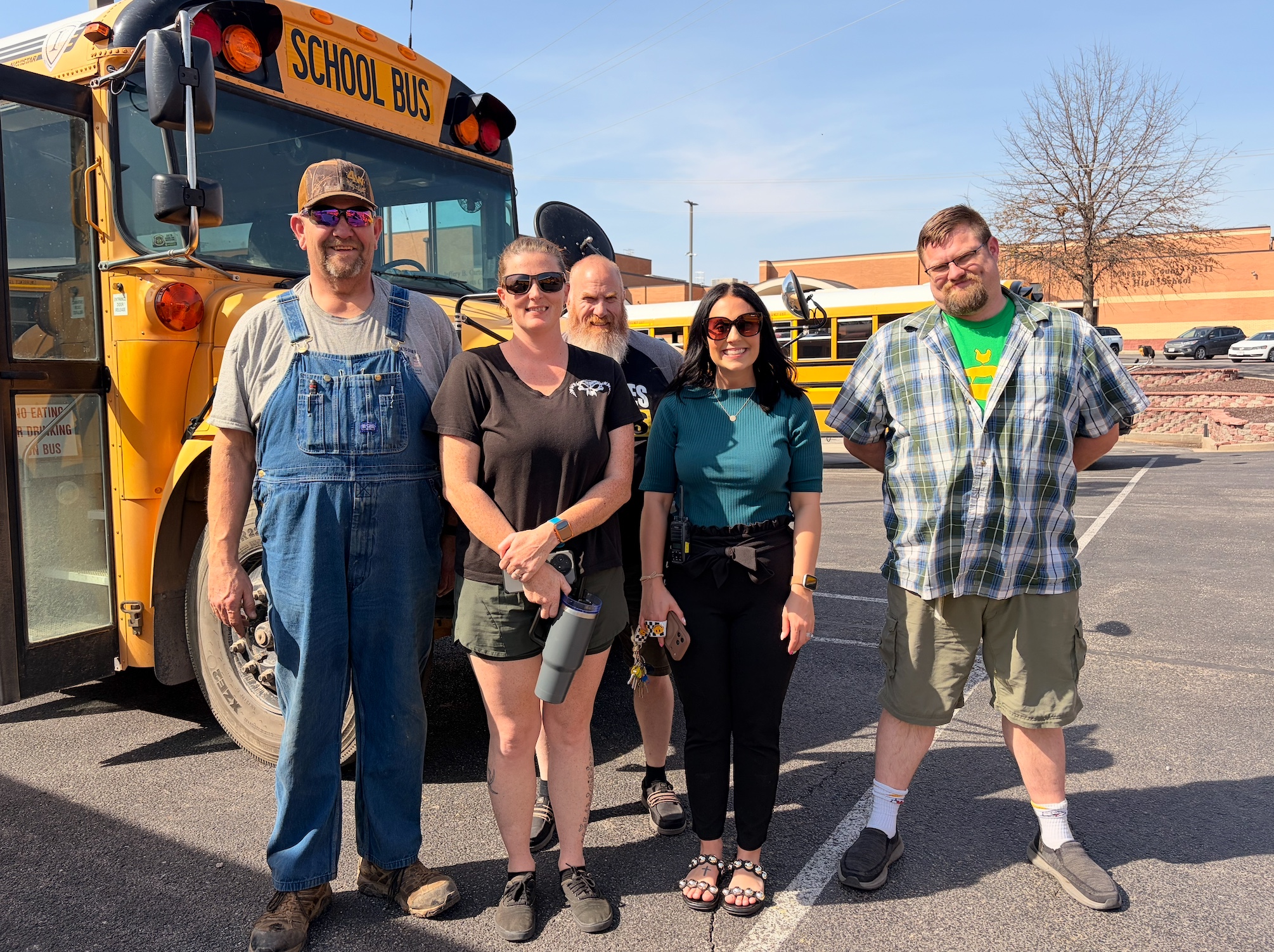 Four adults and one person stand in front of a yellow school bus.