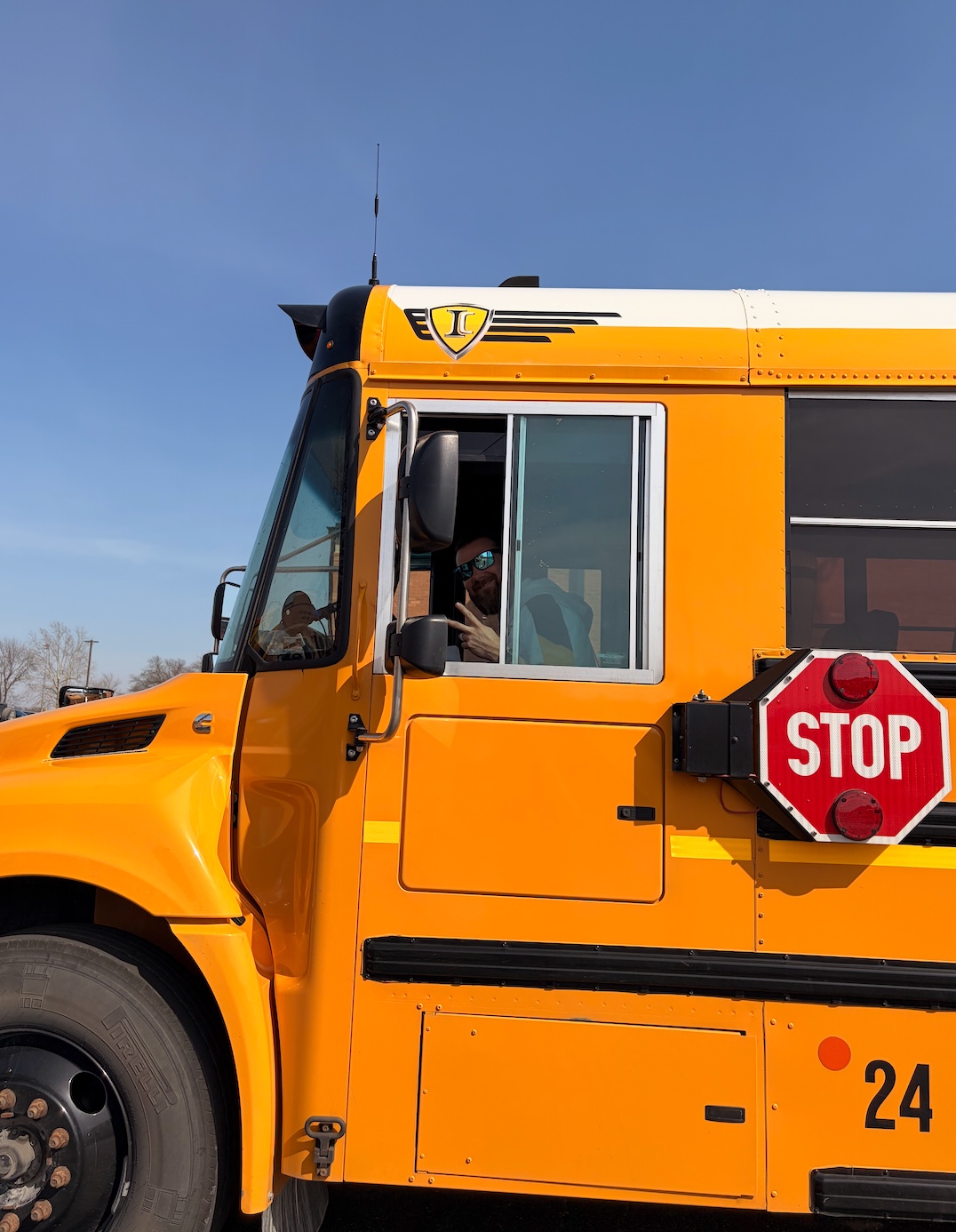 A school bus driver smiles and gives a peace sign from the driver's seat.