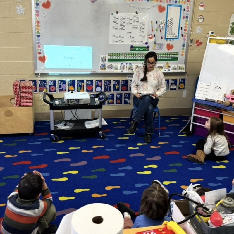 A presenter stands before a group of young students. 