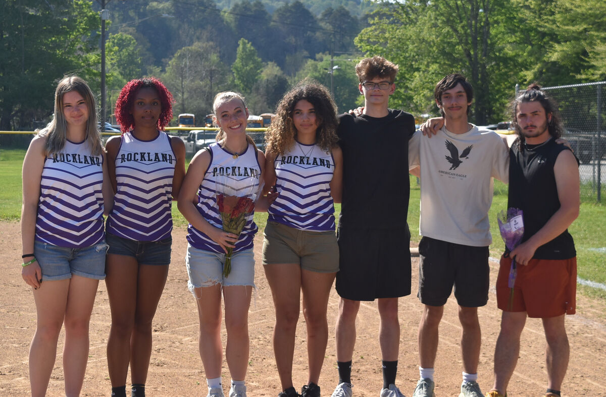 A group of young people, some wearing 'ROCKLAND' athletic tops, stand together on a dirt field.