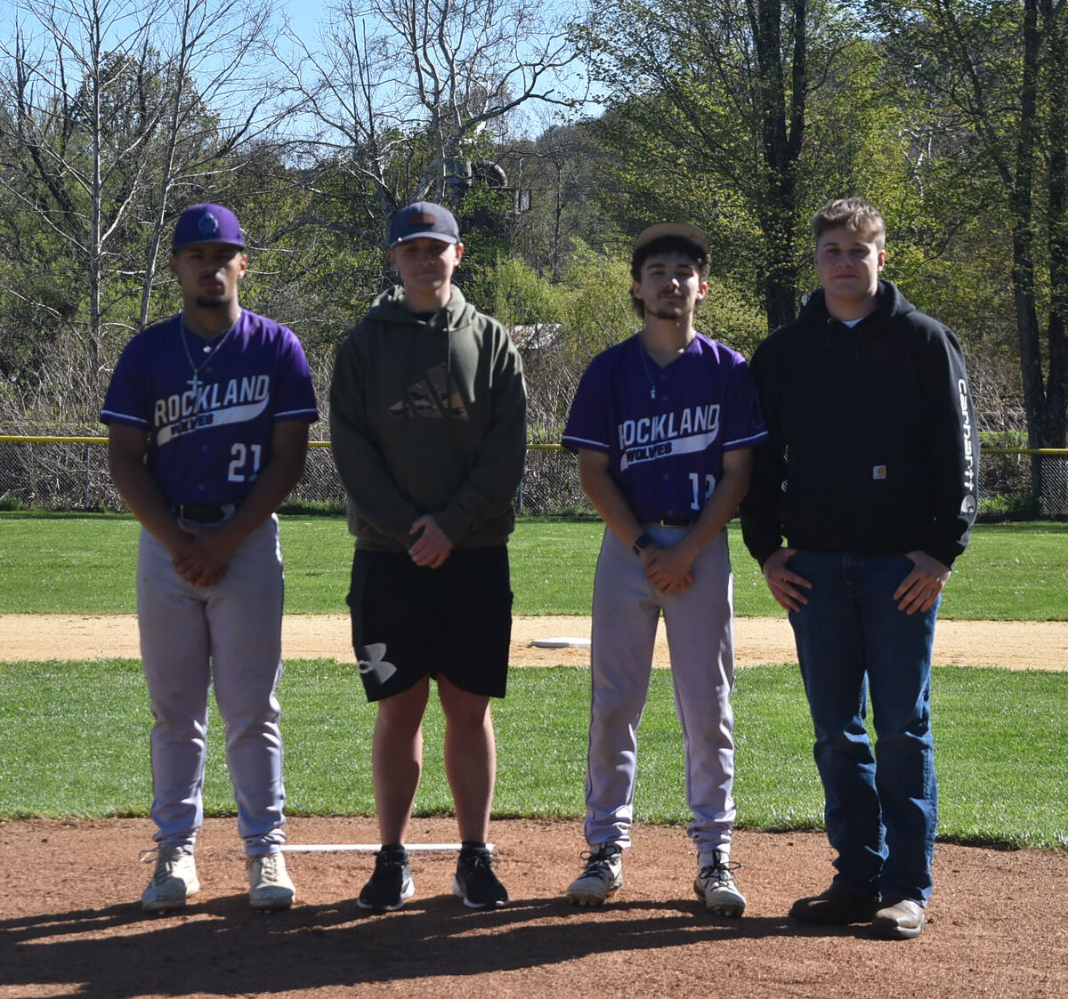 Four young men stand on a baseball field, two in purple "ROCKLAND WOLVES" jerseys.