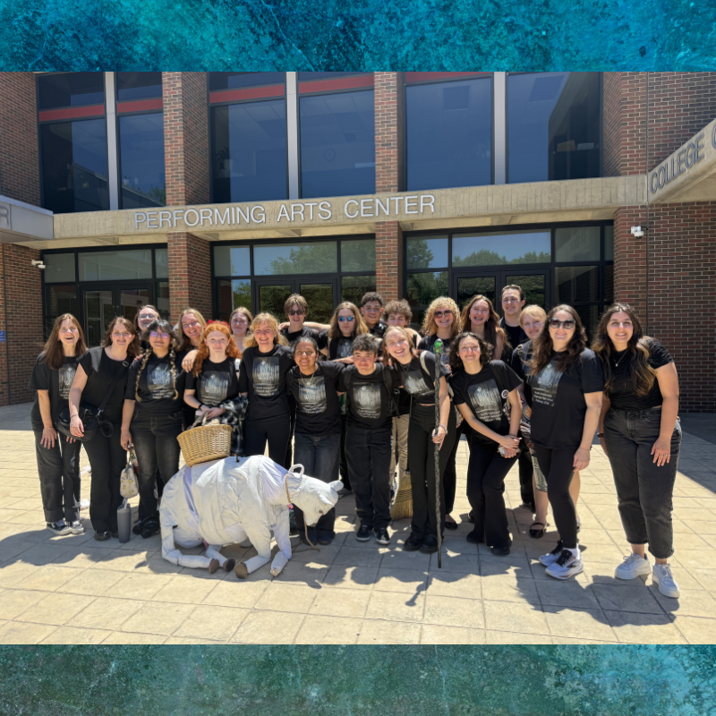 A group of young people in matching black t-shirts pose with a white prop animal outside a Performing Arts Center.