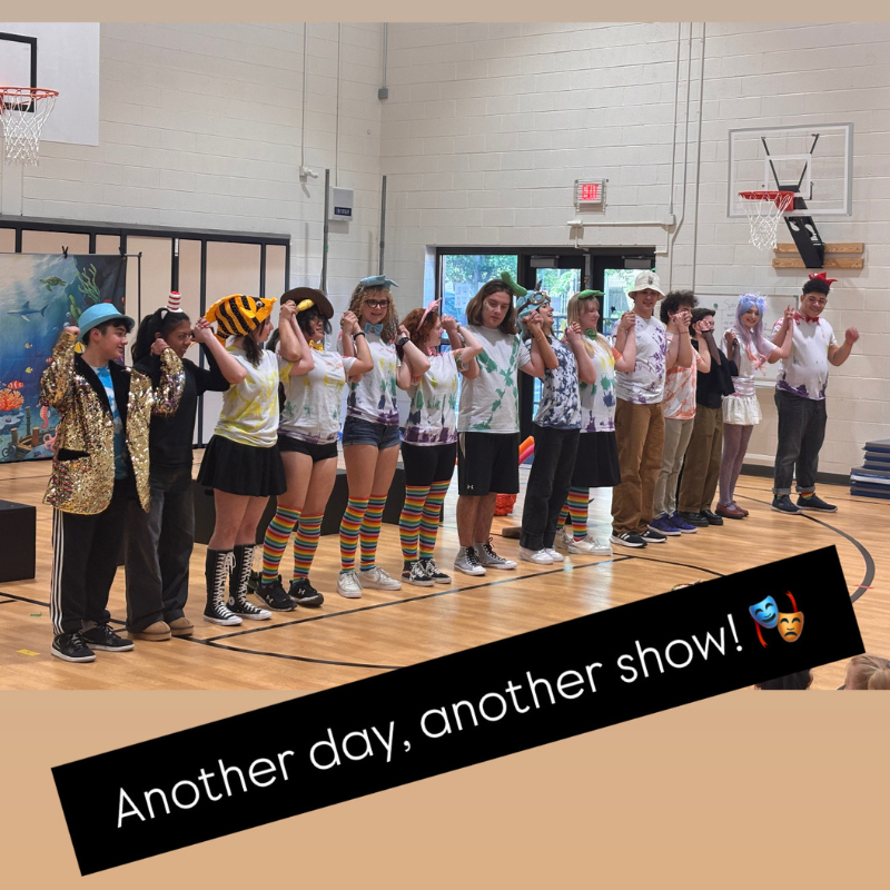 A group of young performers in colorful costumes stand in a line, holding hands.