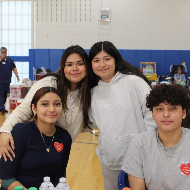 Four young people smile for a photo at what appears to be a community event or donation drive.