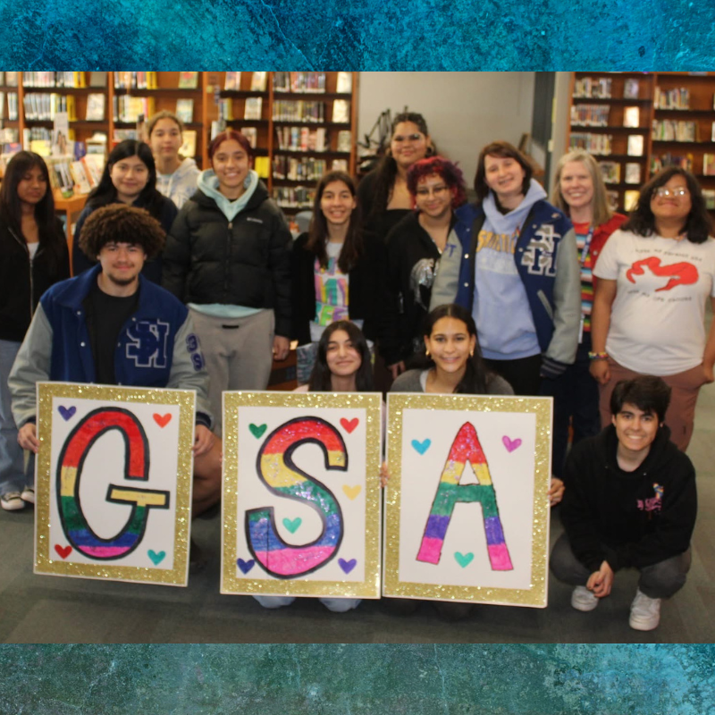 A diverse group of students poses for a photo, holding signs that spell out 'GSA' with rainbow colors.