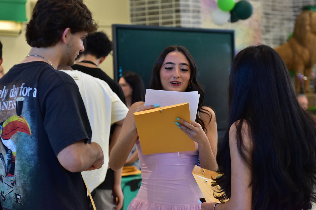 A young woman in a pink dress smiles as she holds papers and an orange folder.