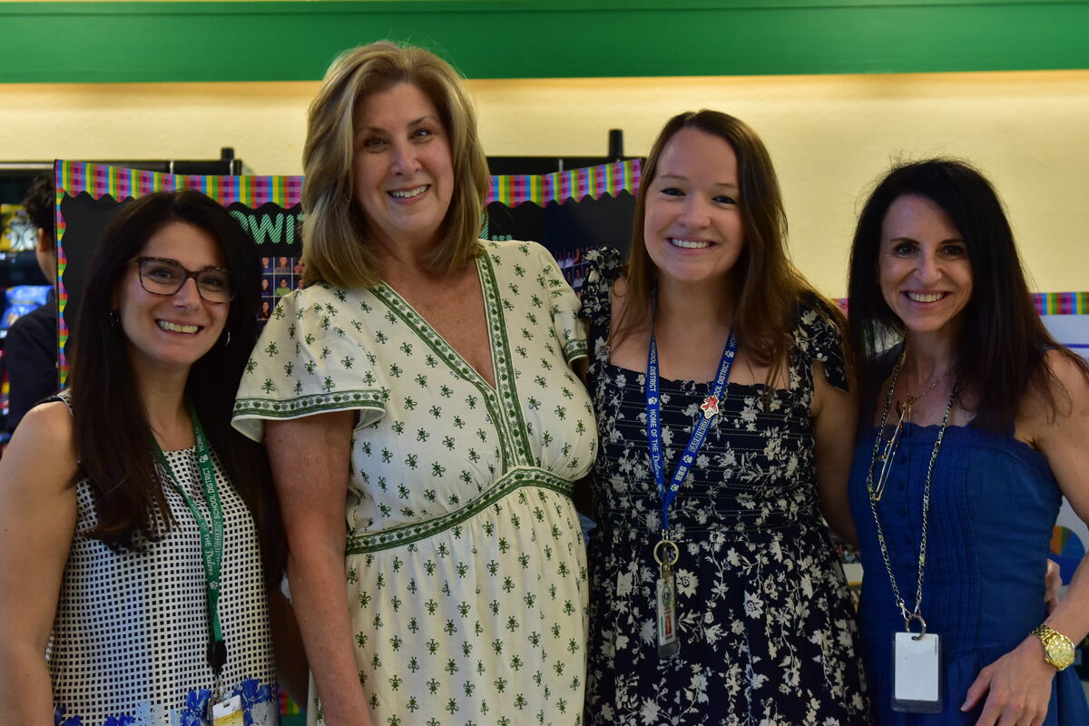 Four smiling women stand together, posing for a photo indoors.