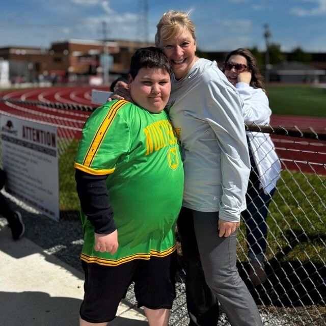 A young person in a green shirt and an adult woman smile while standing next to a track.