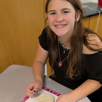 A young person smiles warmly while working on a clay project at a table.