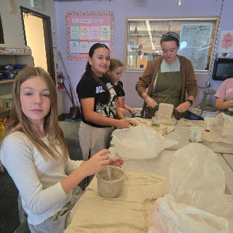 Students and an instructor work on clay projects at tables in an art classroom.