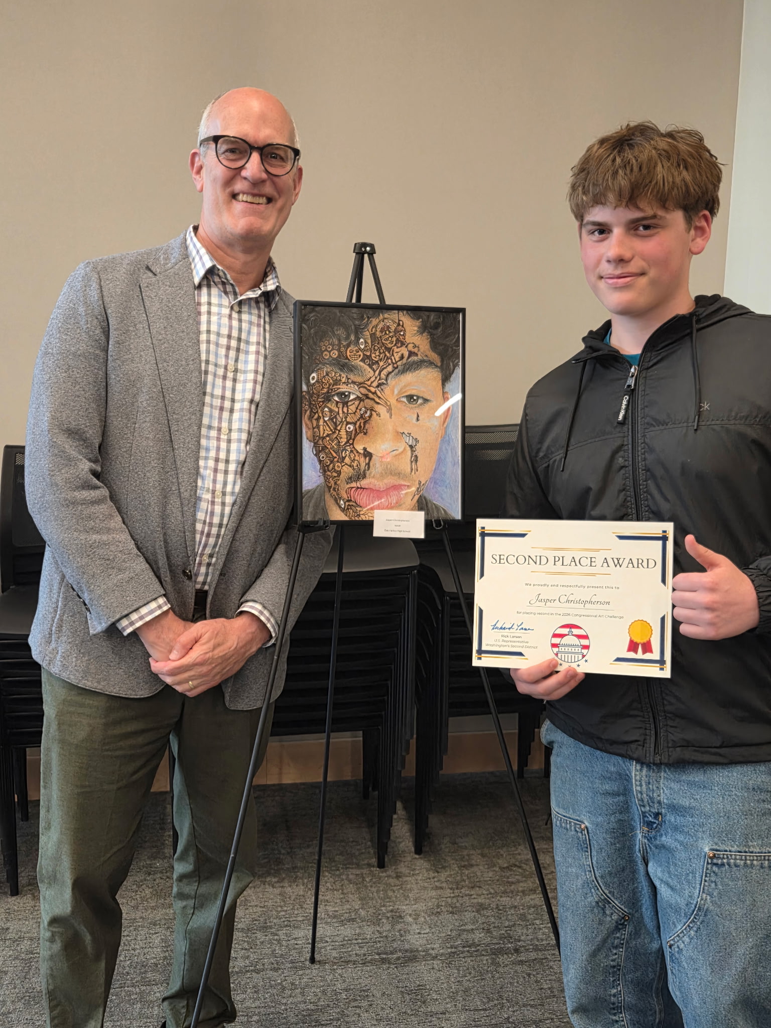 A man in a blazer and a young man in a jacket stand next to an artwork and a second place award certificate.