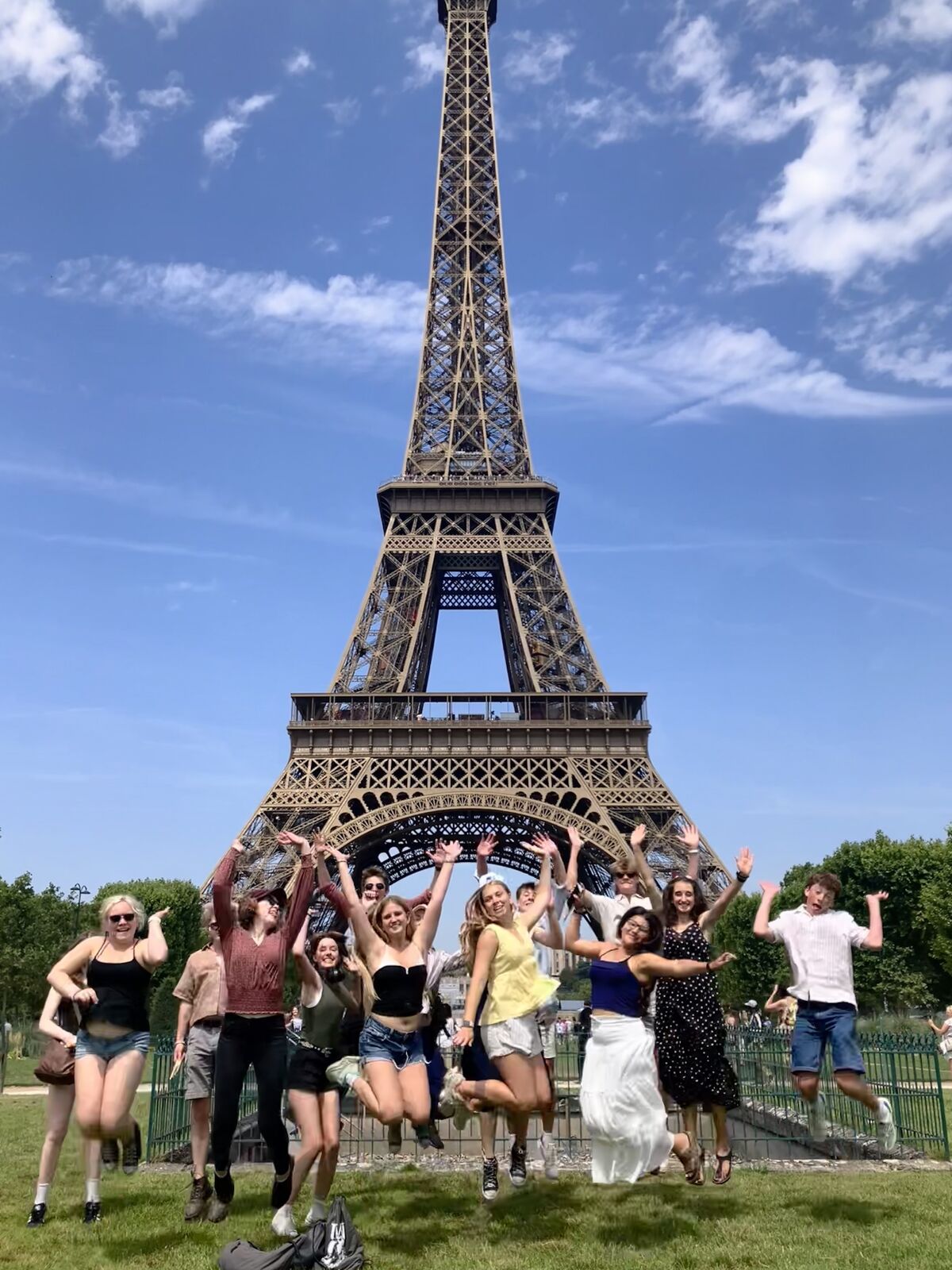 A group of friends jumps joyfully in front of the Eiffel Tower on a sunny day.
