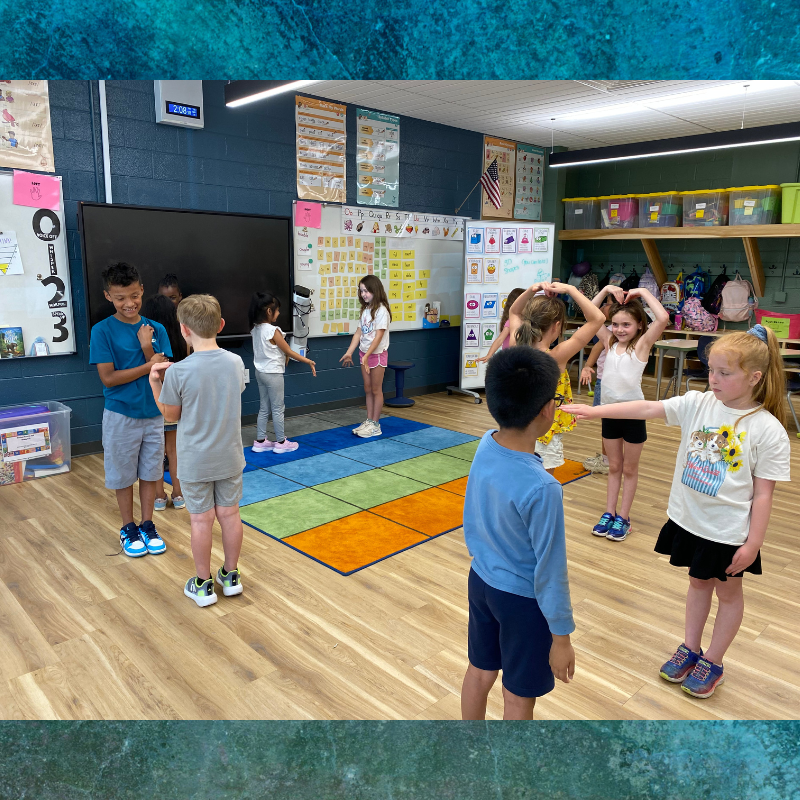 Children participate in a classroom activity, standing on a colorful rug.