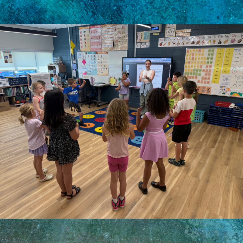 A teacher leads a group of young students in a circle activity in a bright classroom.