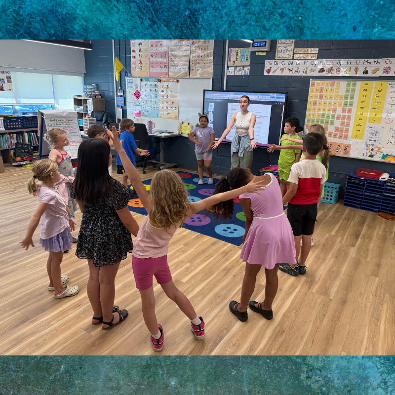 A teacher leads a group of young students in an activity in a brightly lit classroom.