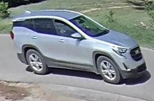 A silver GMC SUV is parked on a paved road with grassy areas in the background.