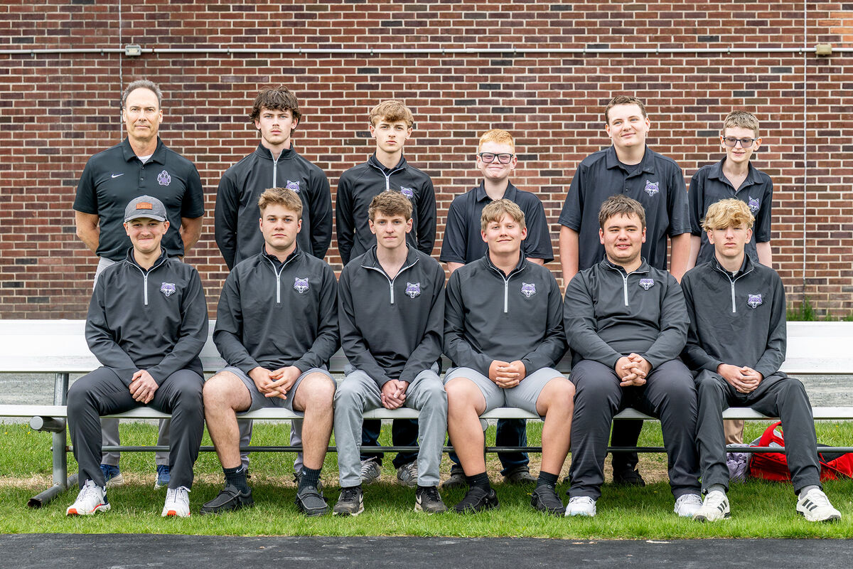 A group of young men and one adult male pose for a team photo in front of a brick wall.