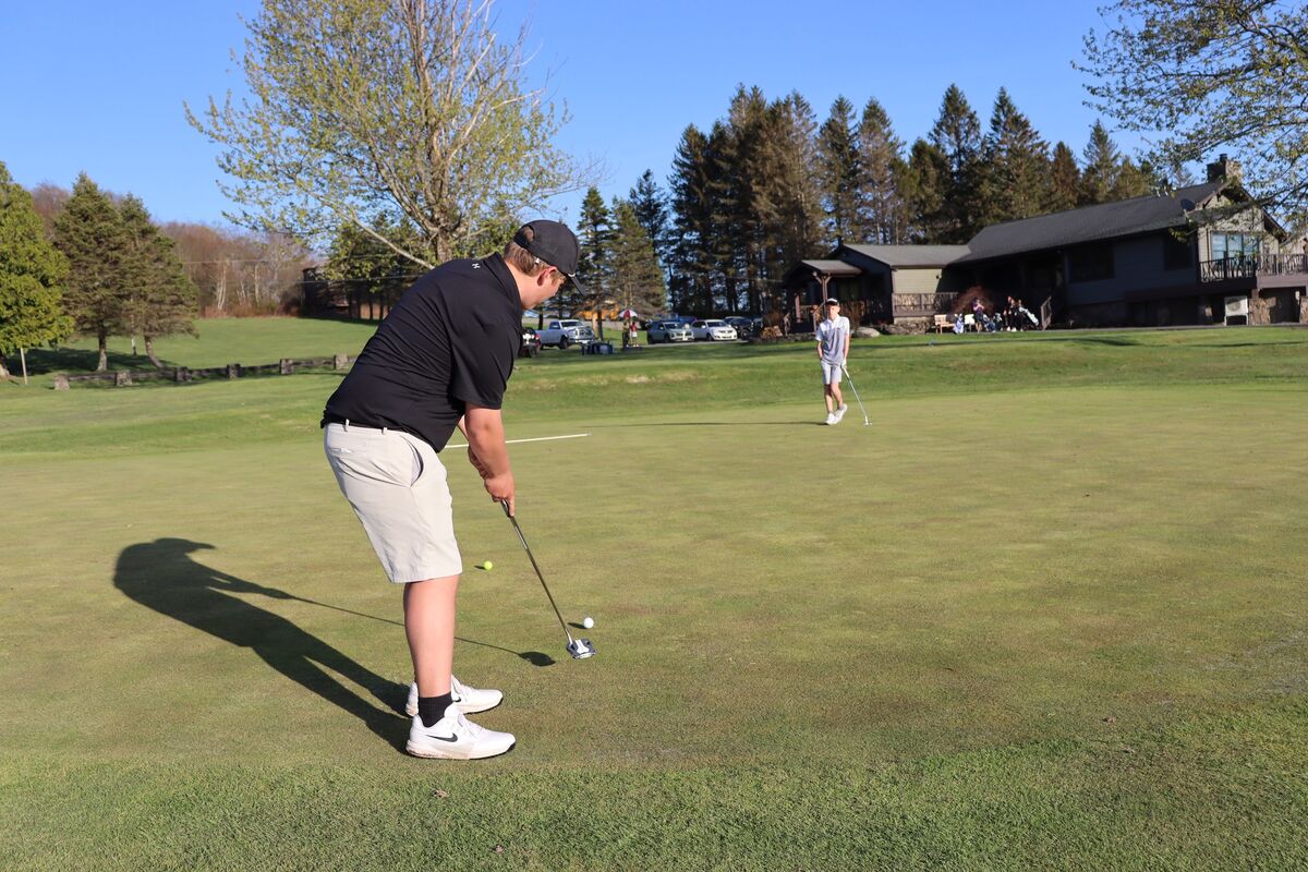 A young golfer in a black shirt and light shorts prepares to putt on a green golf course.