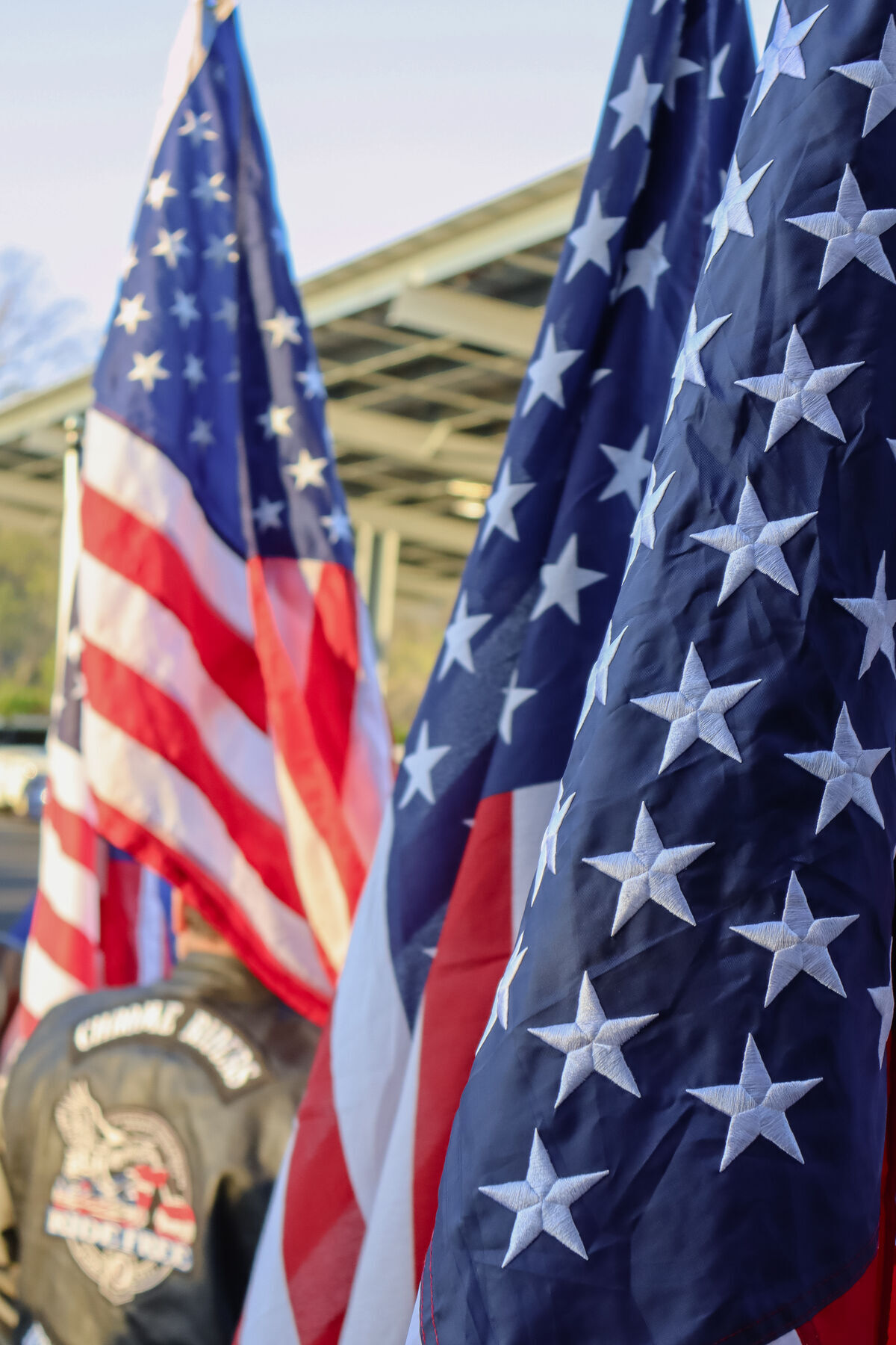 Several American flags wave gently in front of a covered structure outdoors.