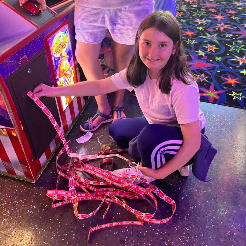 A young girl smiles as she collects a long string of red tickets from an arcade game.