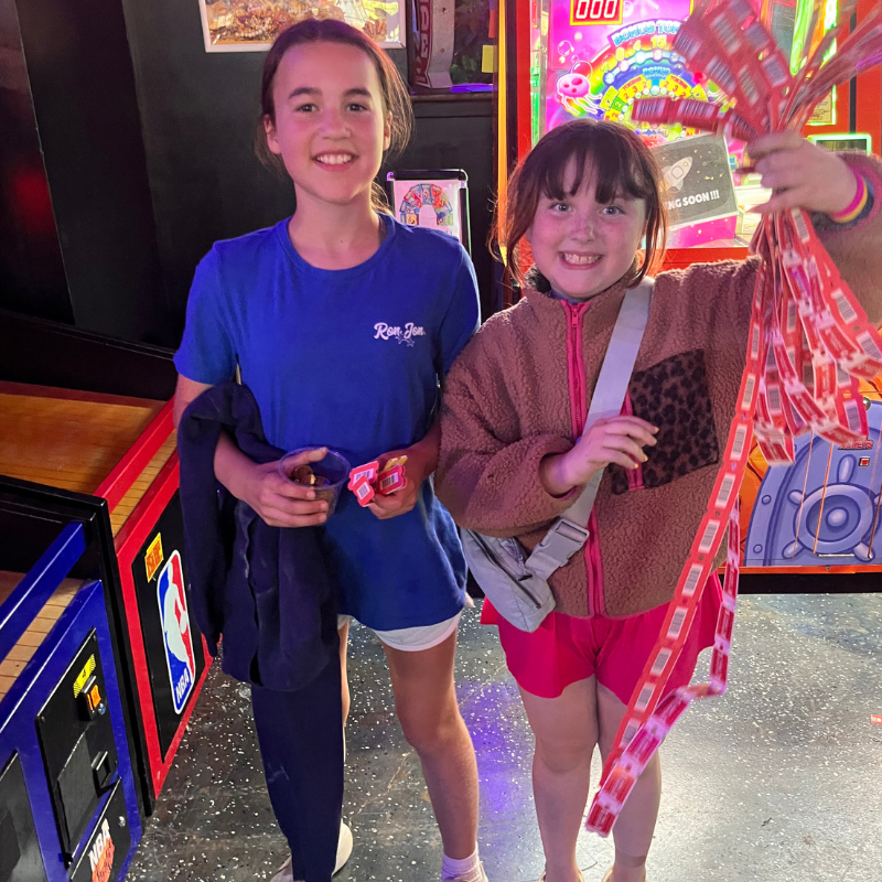 Two smiling girls hold a large bunch of tickets, likely from an arcade.