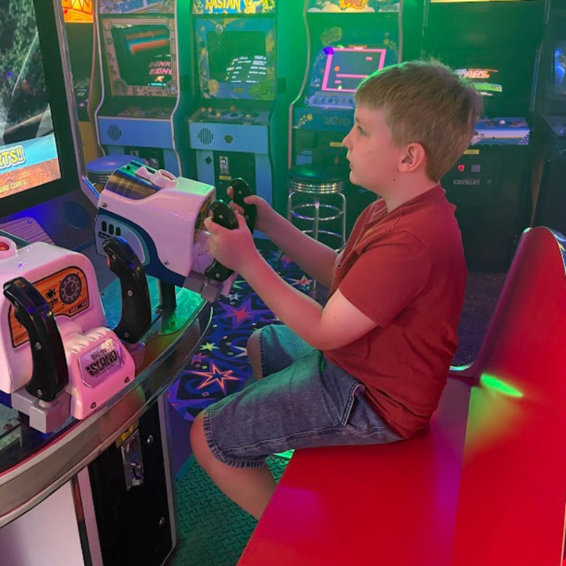 A young boy plays an arcade game, gripping the controls with focus.