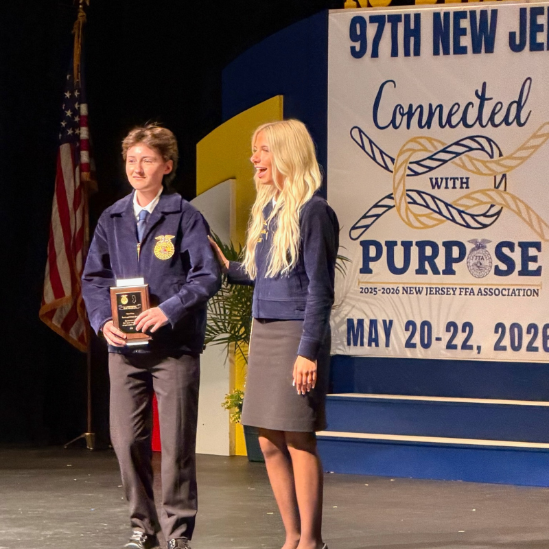 A young person in an FFA jacket receives an award on stage, with a woman standing beside them.
