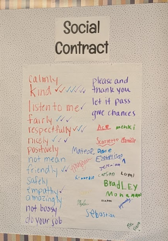 Handwritten "Social Contract" poster on a bulletin board featuring student-suggested values like "kind," "respectfully," "empathy," and "give chances," signed with student names in colorful markers.