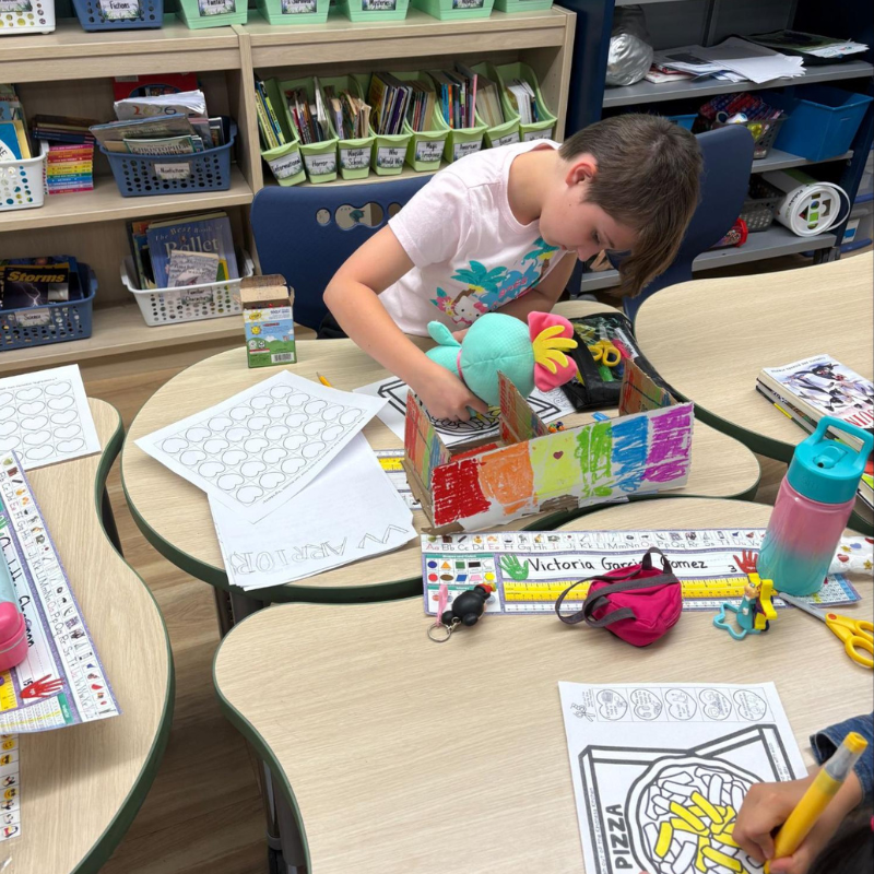 A child is focused on a colorful, handmade cardboard creation in a classroom setting.