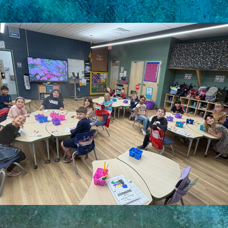 A classroom of young students sits at colorful tables, engaged in an activity.